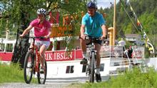 Bilde av to syklister med Henrik Ibsen i bakgrunn - Klikk for stort bilde